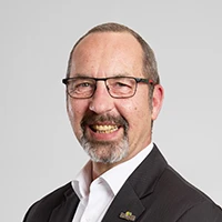 Thomas Schön, im Anzug und mit Brille, lächelndes Porträtfoto vor hellem Hintergrund.