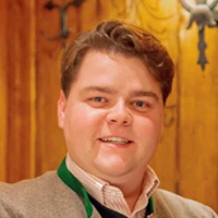 Leopold Schilling, Geschäftsführender Direktor und Prokurist der Kuffler Gruppe München, im Porträt vor holzvertäfeltem Hintergrund.