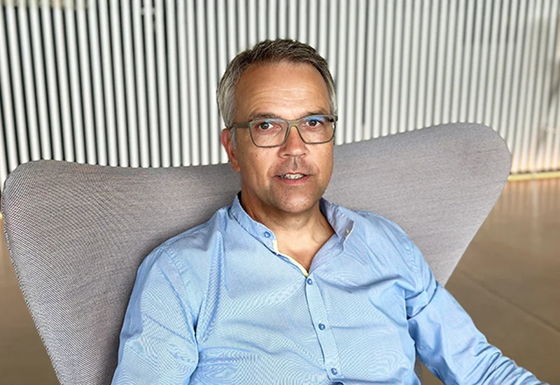 Torsten von Borstel, Geschäftsführer, im Porträt auf einem modernen grauen Sessel vor gestreiftem Hintergrund.