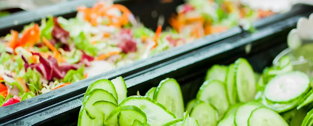 Frische Salatbar in der Betriebskantine mit Gurken, Blattsalat, Karotten und buntem Gemüse – gesundes Essen für Mitarbeitende.